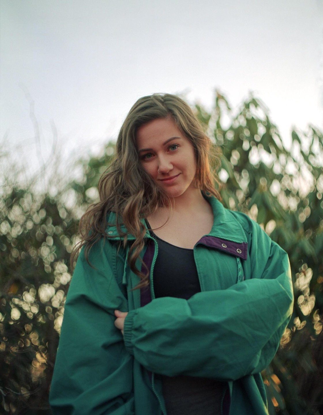 A woman with long wavy hair and a green jacket smiles at the viewer.