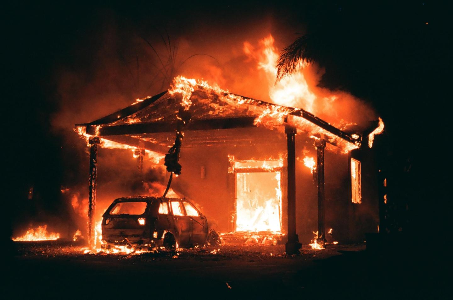 A house and a car are engulfed in flames at night.