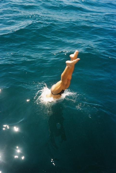 A person dives into the ocean, with their legs and feet visible above the water as they create a splash.