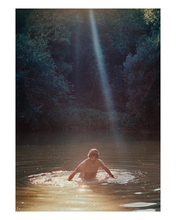 A man stands in a body of water with a beam of light shining down from above.