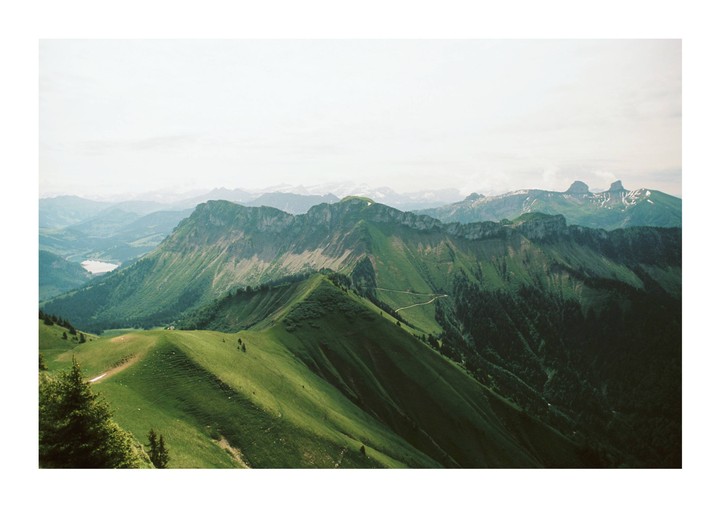 A vast mountain landscape with green slopes and distant peaks under a bright sky.