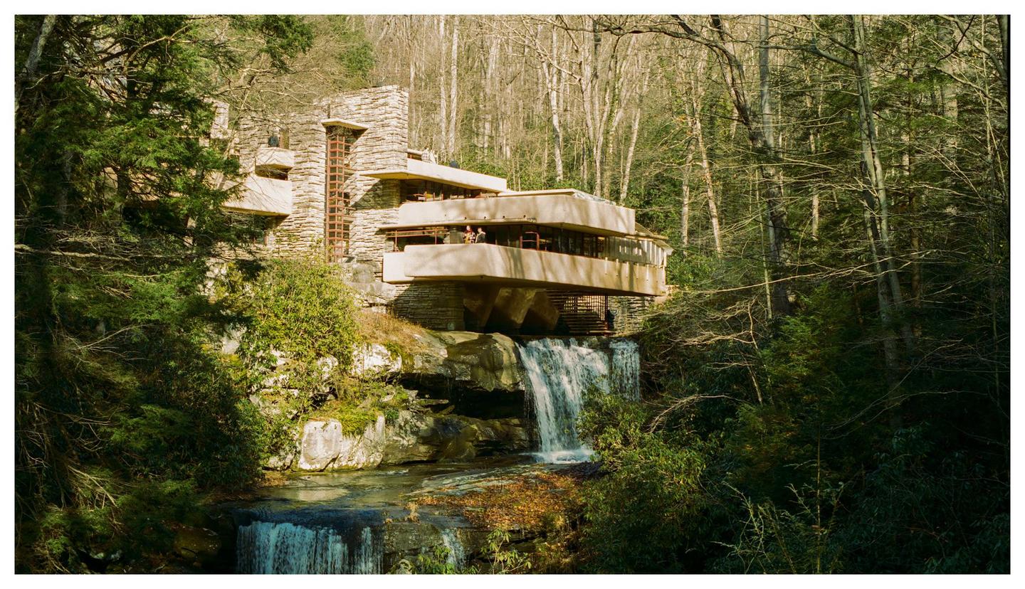 A house with multiple balconies is built over a waterfall in a forest.