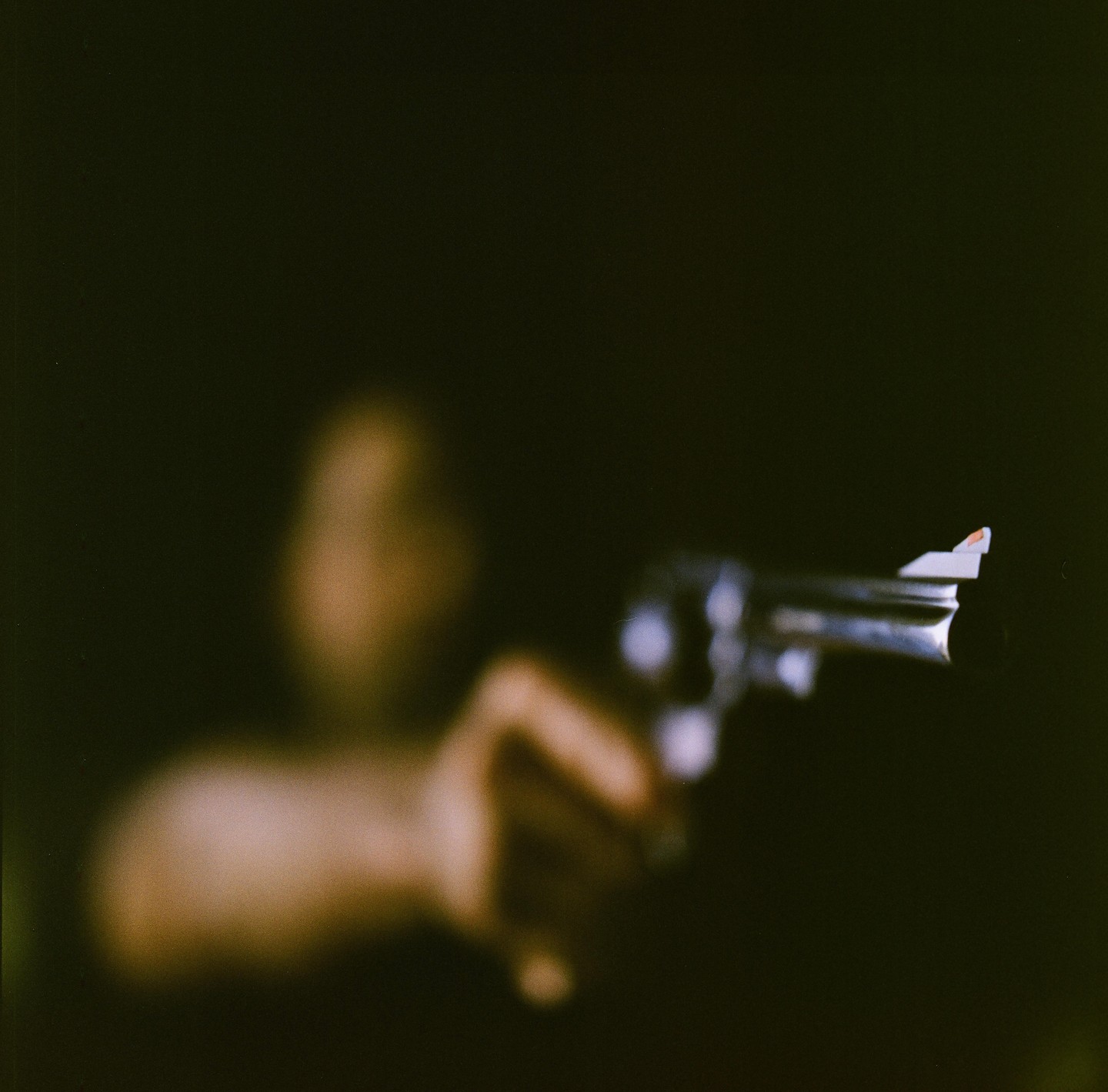 A blurry hand holds a revolver pointed towards the viewer in a dark setting.