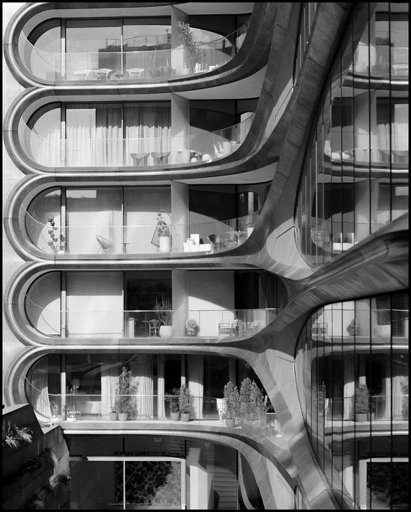 A modern building with five balconies and curved architectural details is shown in black and white.