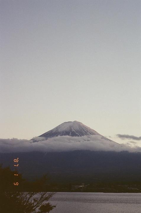 Mount Fuji is visible with its snow-capped peak above a layer of clouds, overlooking a body of water.