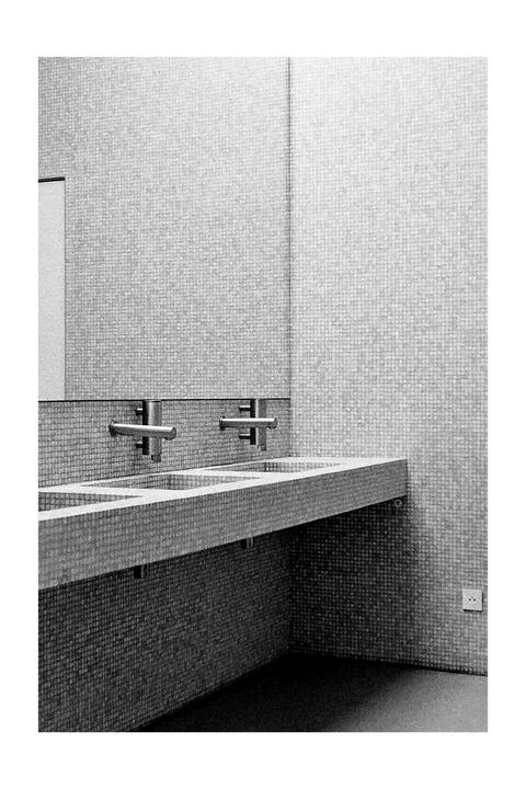 A row of sinks with wall-mounted faucets is visible in a tiled room.