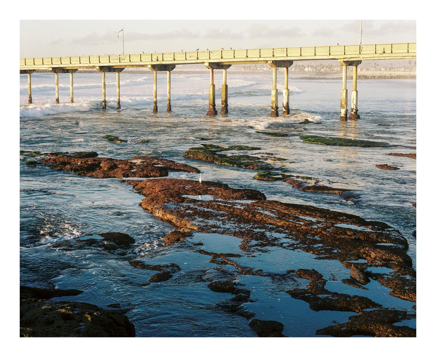 A pier extends over a rocky beach with waves crashing against the shore.