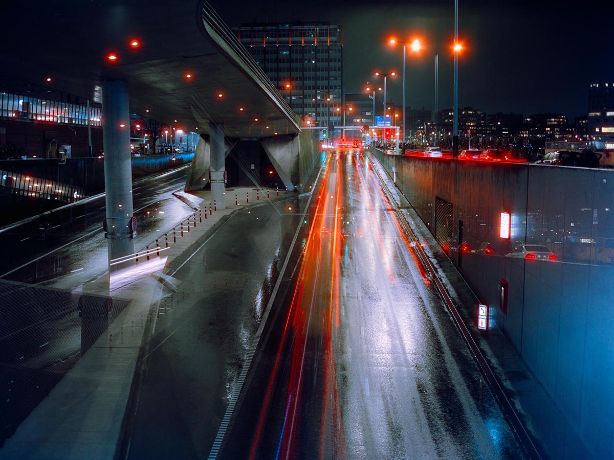 A multi-exposure image shows a highway at night with light trails from vehicles and reflections on the wet road.