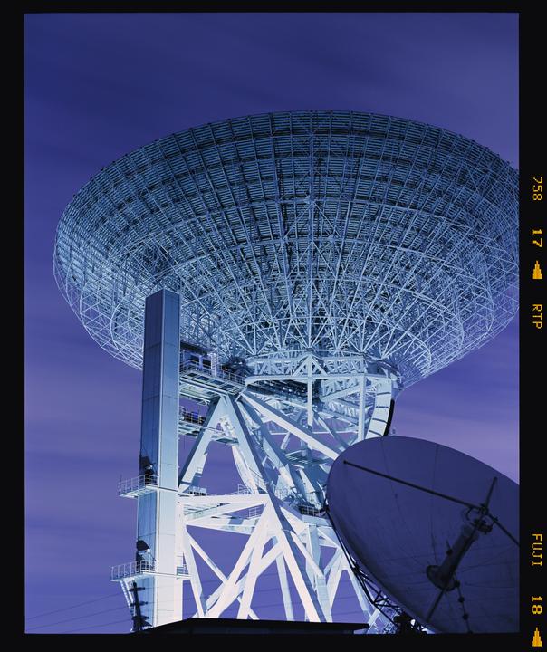 A large satellite dish and its support structure are visible against a purple sky.