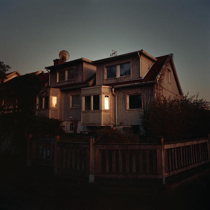 A large house with light shining from its windows is seen at dusk.