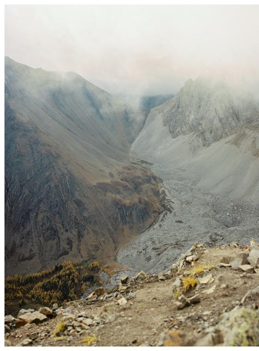 A misty mountain valley with a rocky riverbed and autumn trees is visible from a high vantage point.