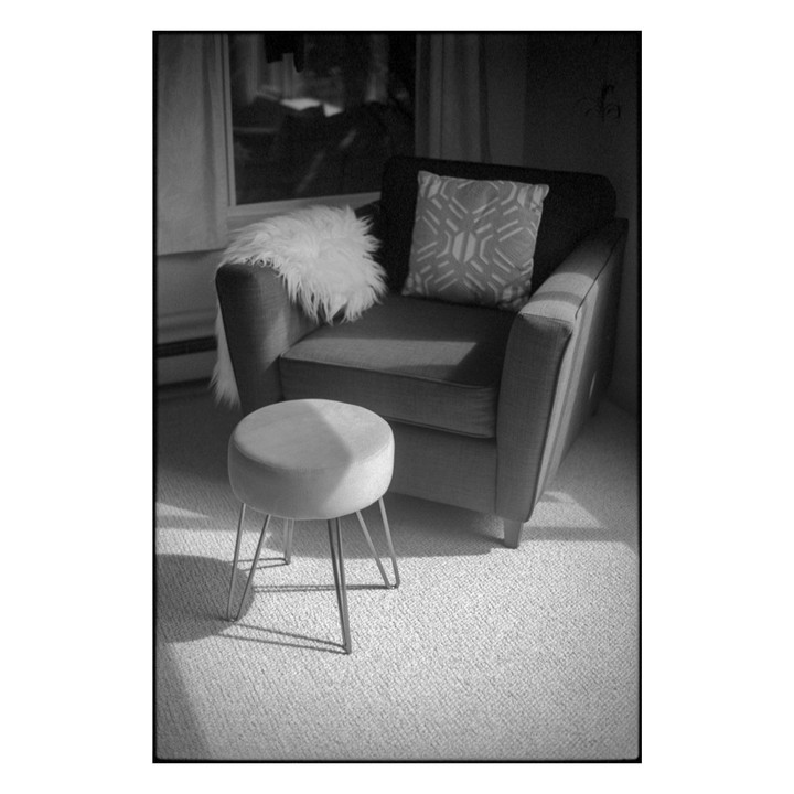 Sunlight illuminates a stool and an armchair with a pillow and a fur throw.