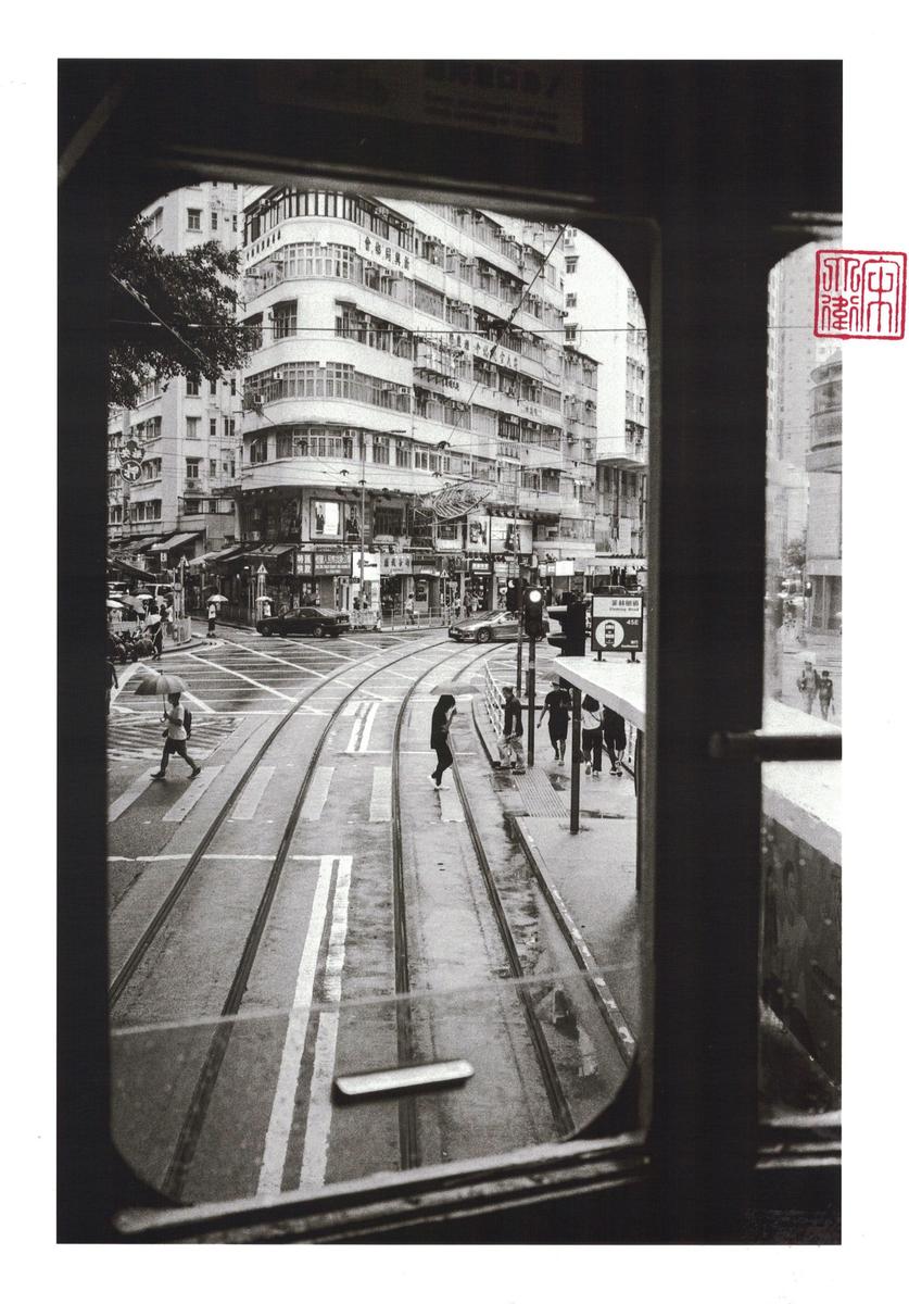 A street with tram tracks and pedestrians is viewed through a tram window.