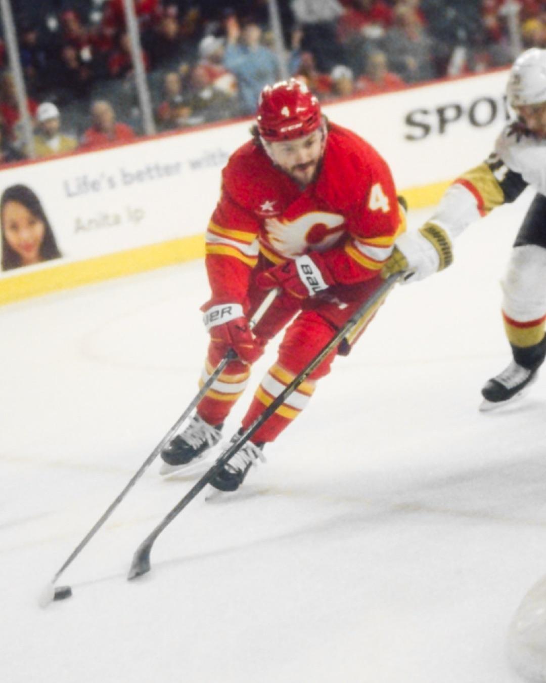 A hockey player in a red uniform skates across the ice with a hockey stick and puck.