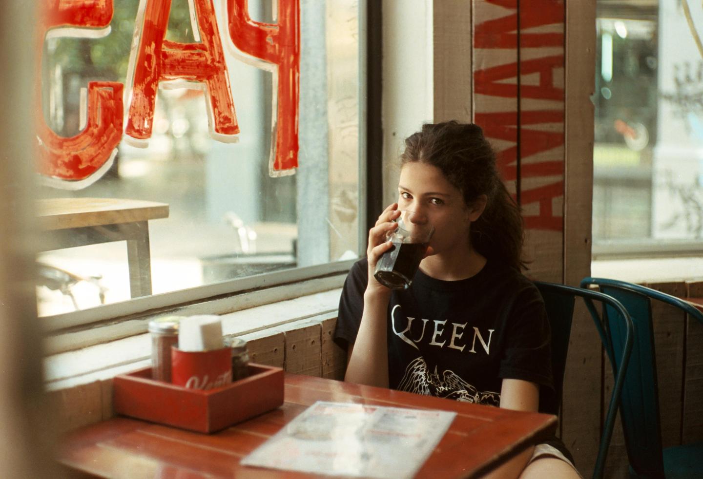 A girl sits at a table in a restaurant and drinks from a glass.