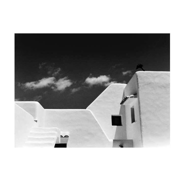 White buildings with geometric shapes are visible under a dark sky with clouds.