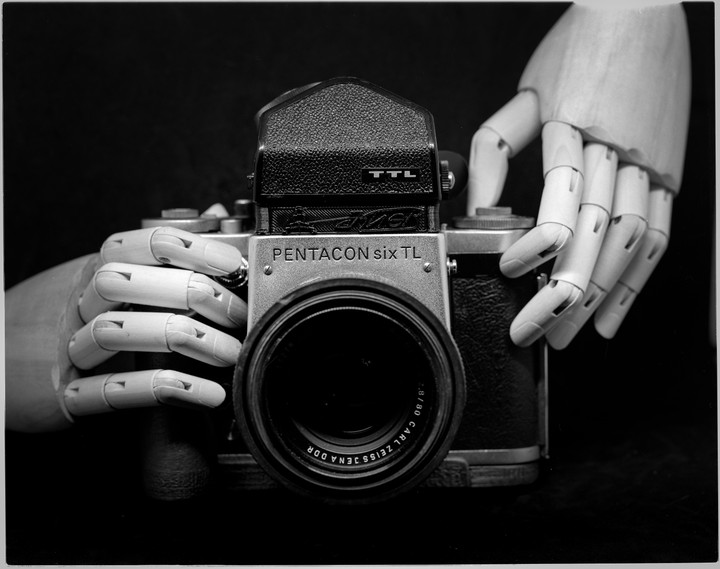 Two wooden mannequin hands hold a Pentacon Six TL camera with a Carl Zeiss Jena lens.