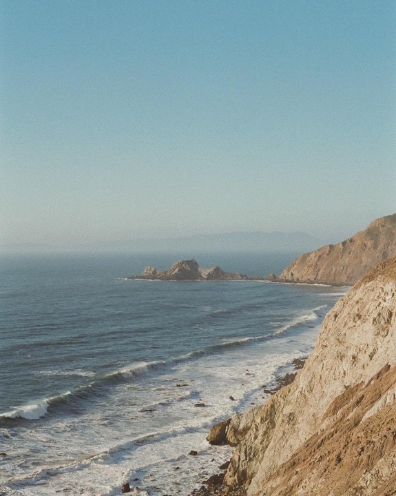 A rocky coastline with waves crashing against the shore under a clear sky.