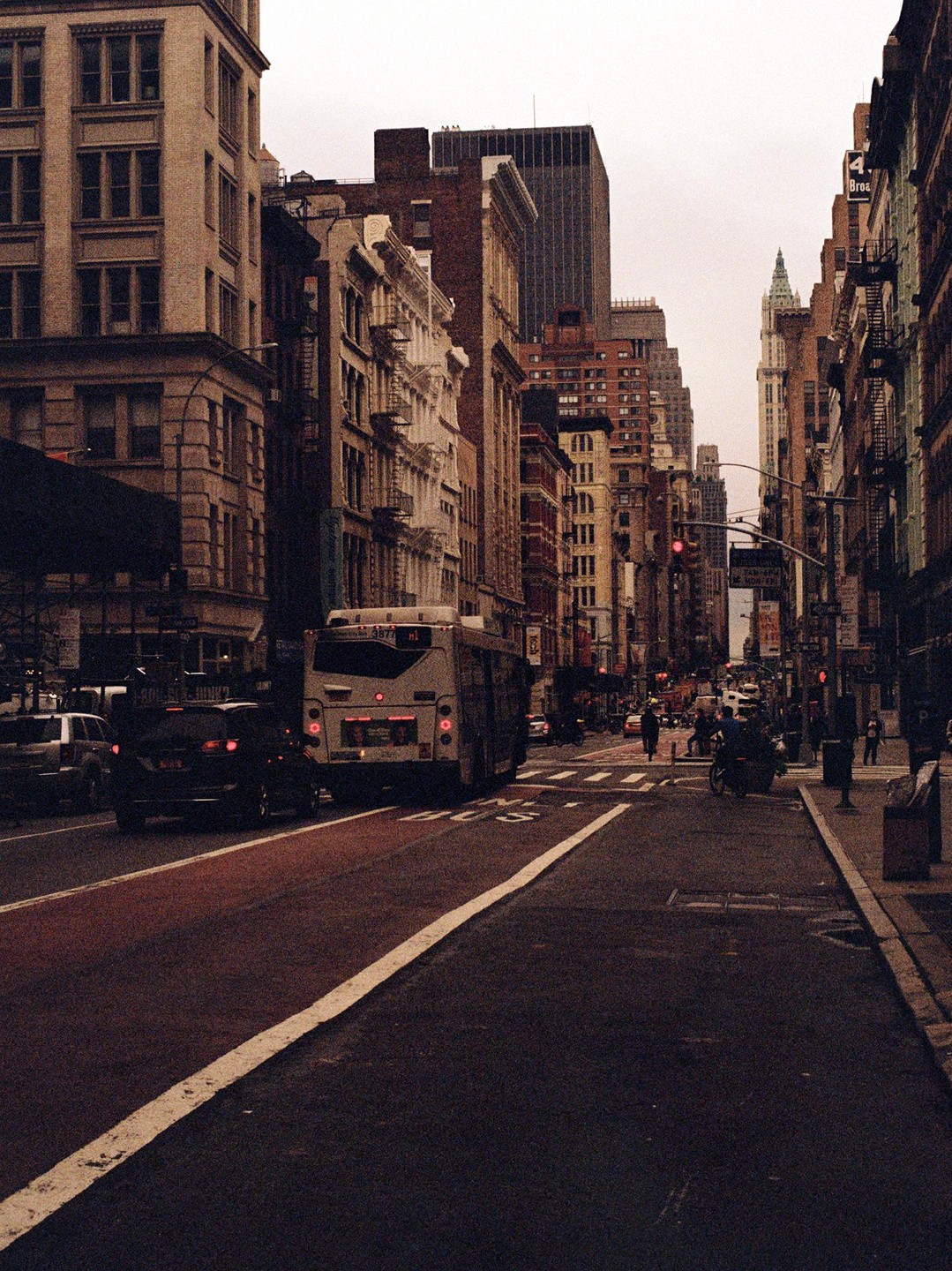 A bus and cars are stopped on a city street lined with tall buildings under an overcast sky.