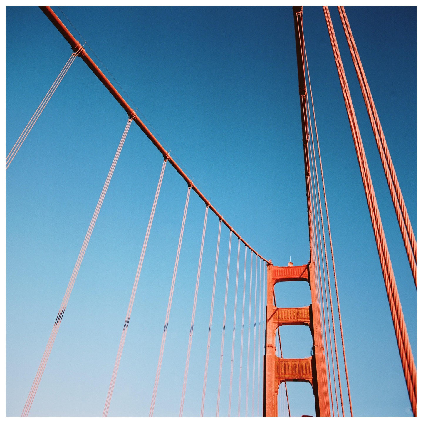 The red cables and tower of a suspension bridge are visible against a clear blue sky.