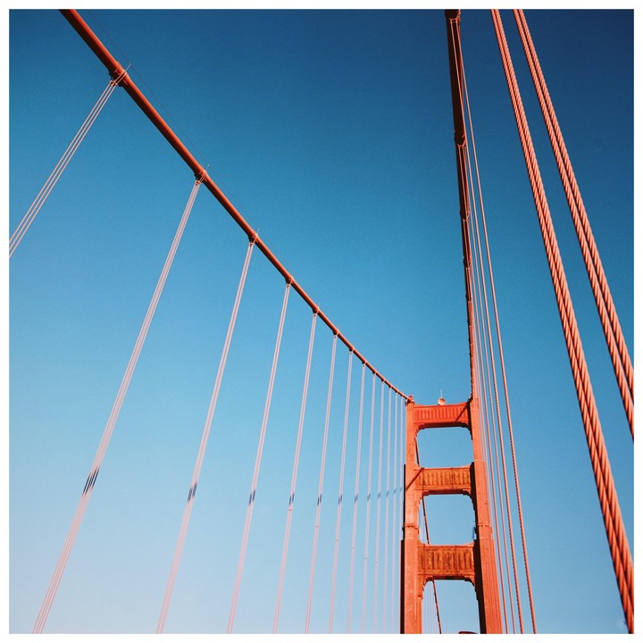 The red cables and tower of a suspension bridge are visible against a clear blue sky.