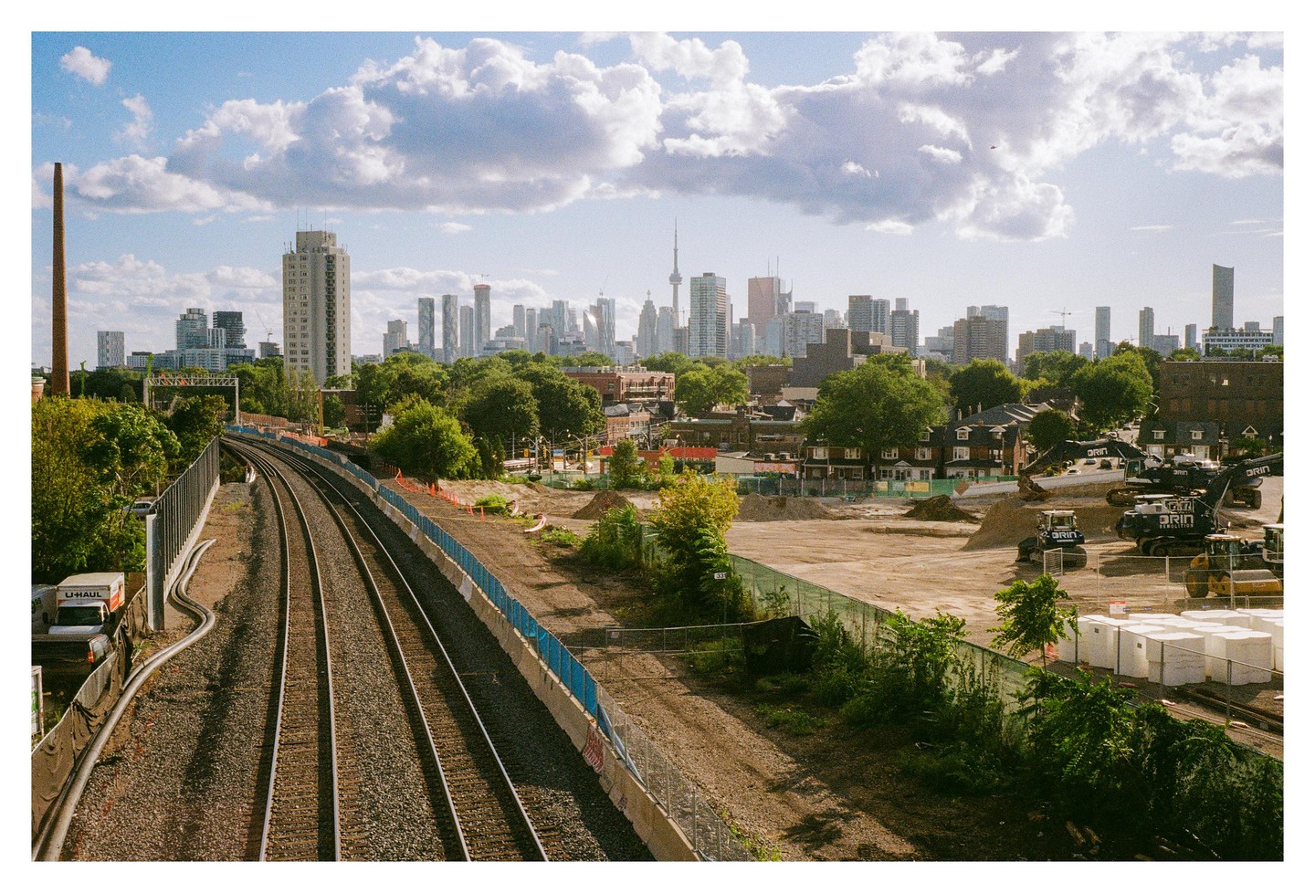 A cityscape with a train track in the foreground and a skyline in the background under a cloudy sky.