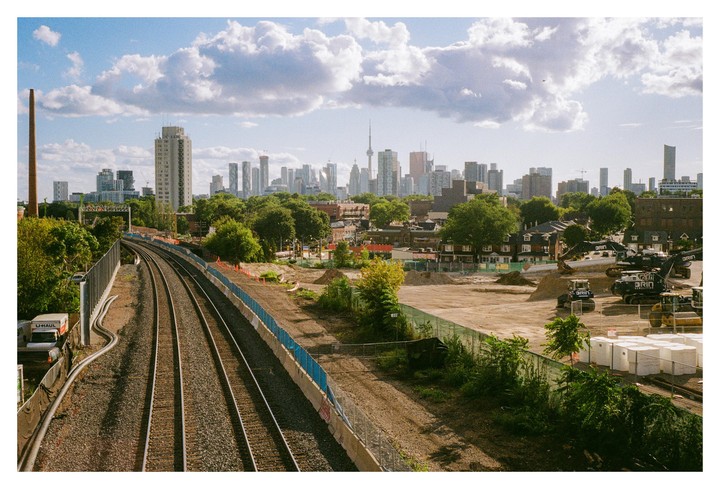 A cityscape with a train track in the foreground and a skyline in the background under a cloudy sky.