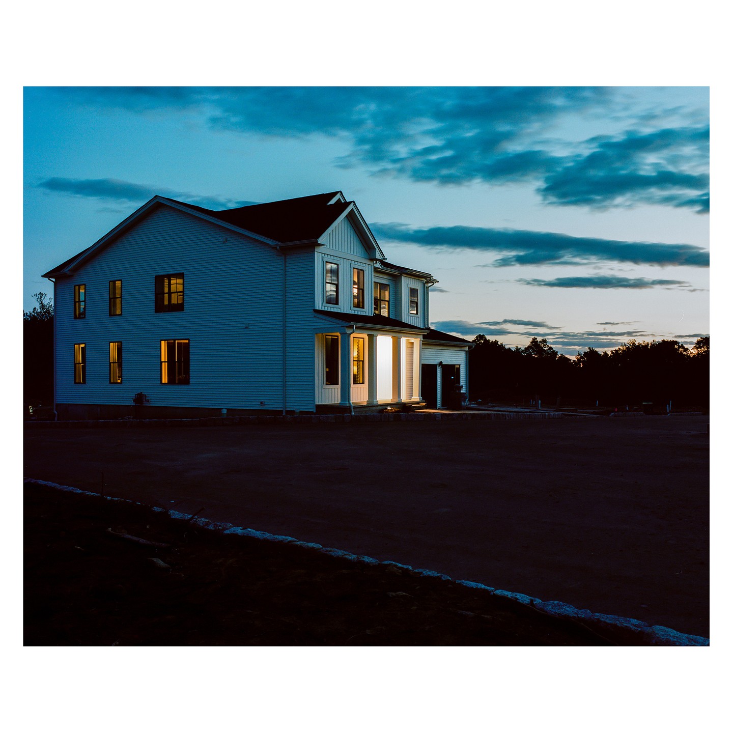 A two-story house with illuminated windows stands under a blue hour sky.