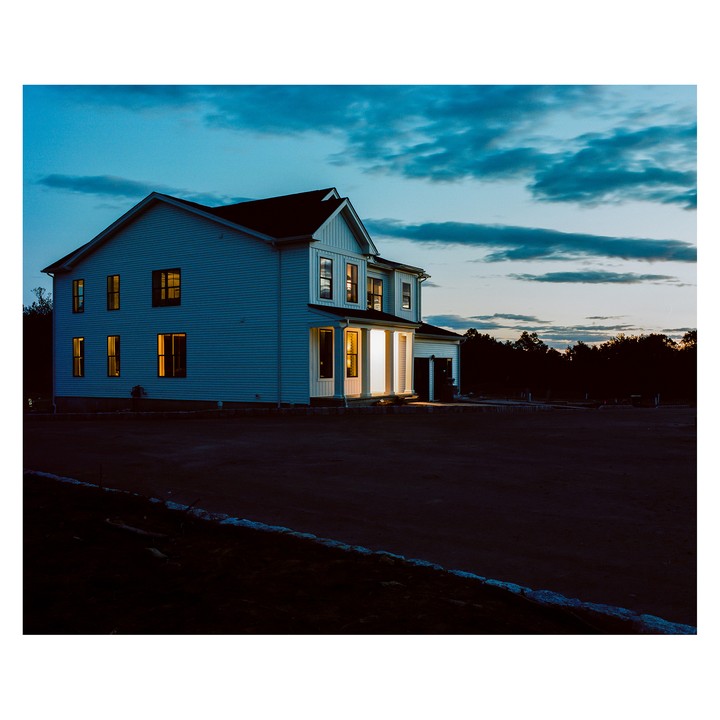A two-story house with illuminated windows stands under a blue hour sky.