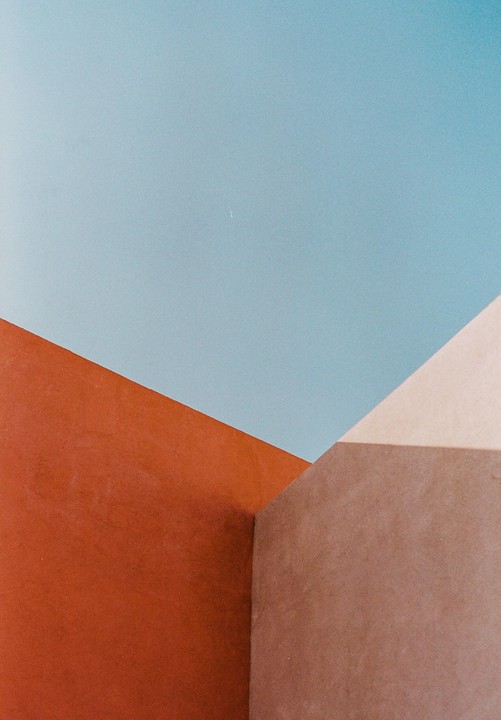 A minimalist composition features geometric shapes in blue, orange, and brown with shadows.
