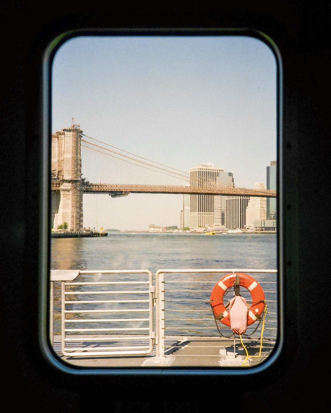 A view of the Brooklyn Bridge and the New York City skyline is framed by a window on a boat.