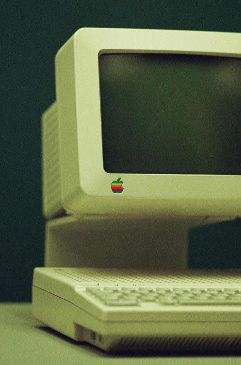A vintage Apple computer monitor with a rainbow logo is visible above a keyboard.