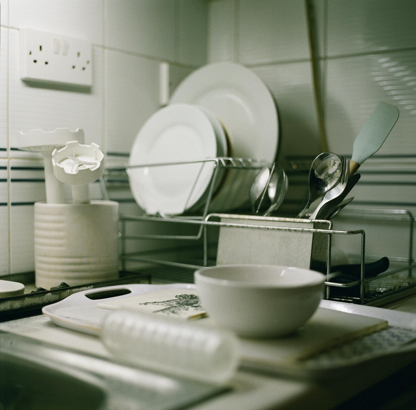 A kitchen sink area is filled with dishes drying in a rack and various kitchen utensils.