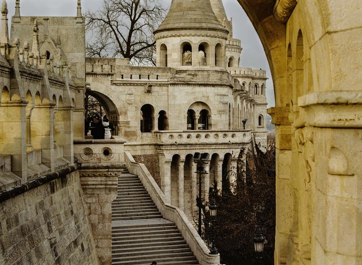 A grand stone staircase leads up to a large, ornate building with multiple towers and arched windows.
