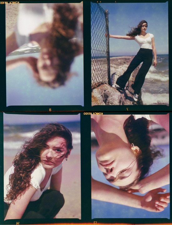A woman with curly hair is shown in four different poses, two of which are reflections, near a fence by the ocean.
