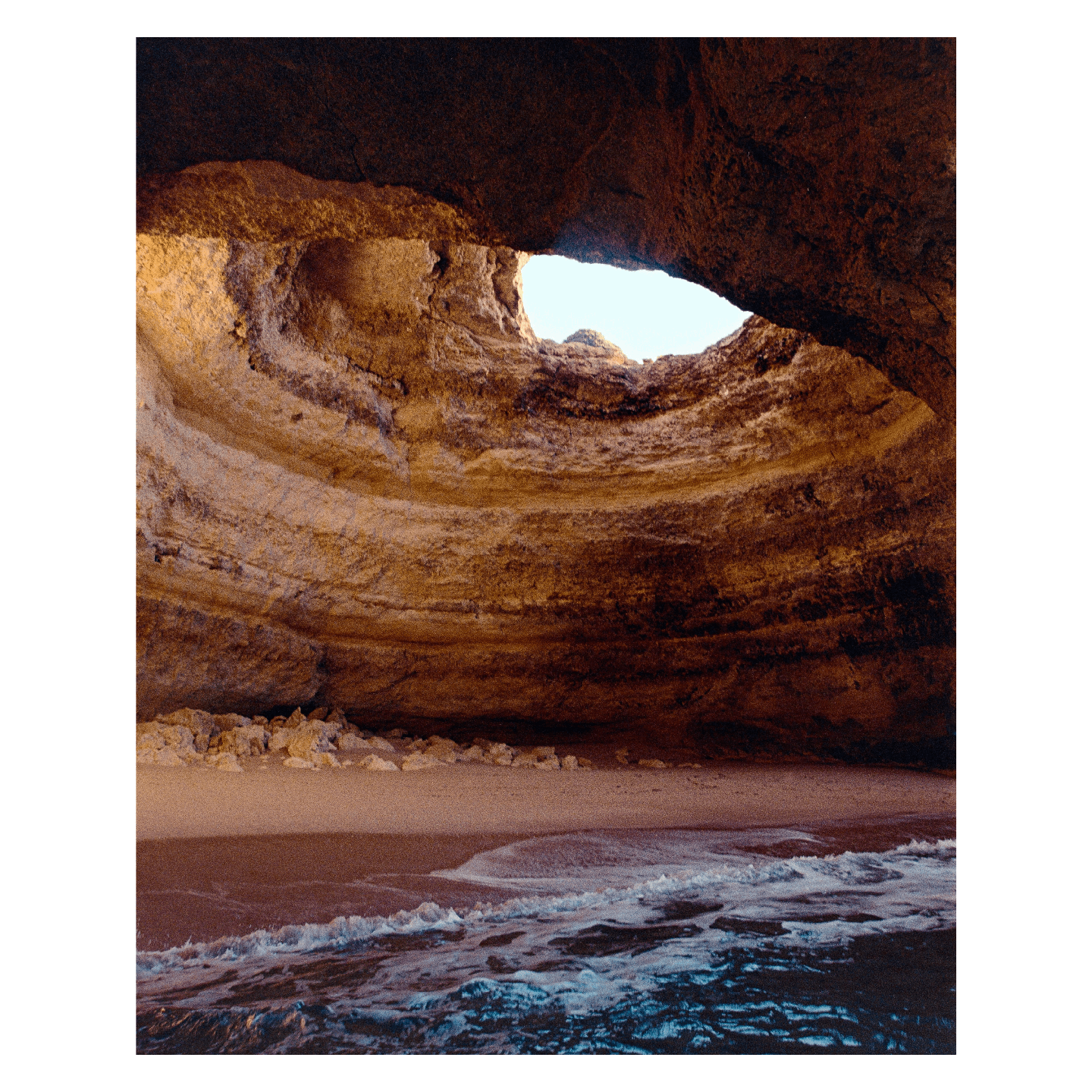A small beach is visible inside a sea cave with an opening in its ceiling.