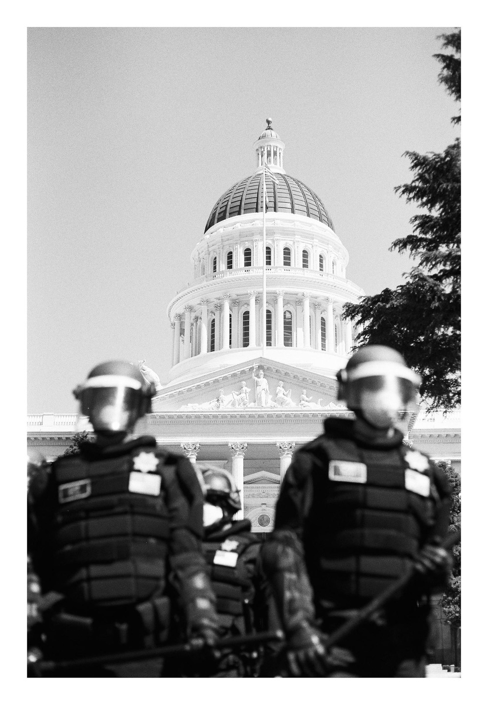 Three police officers in riot gear stand in front of a large domed building.