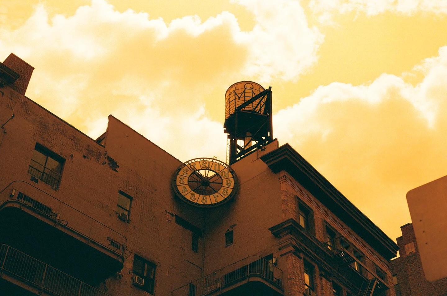 A large clock and a water tower are visible on the roof of a building against an orange sky.
