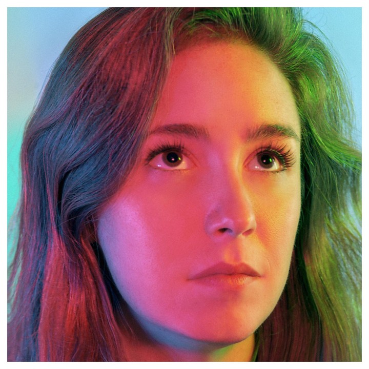 A woman with long hair looks up, illuminated by colorful light.