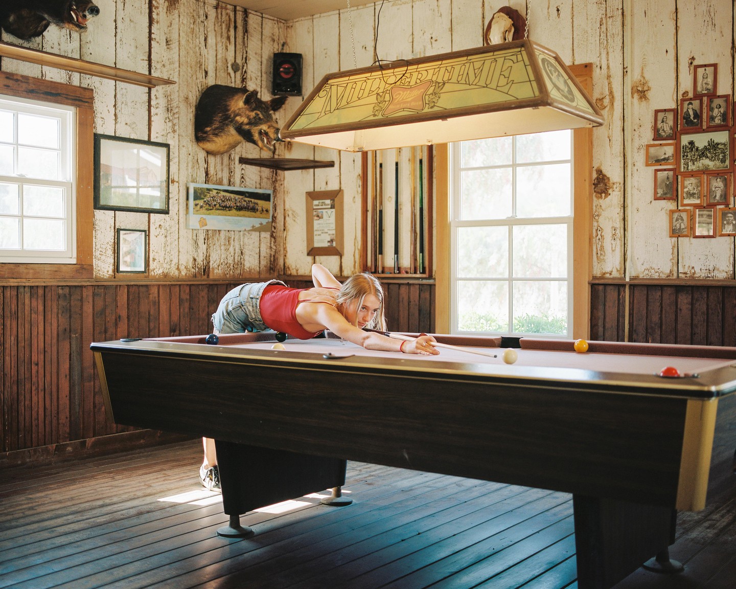 A woman leans over a pool table, aiming a cue stick at a white ball.
