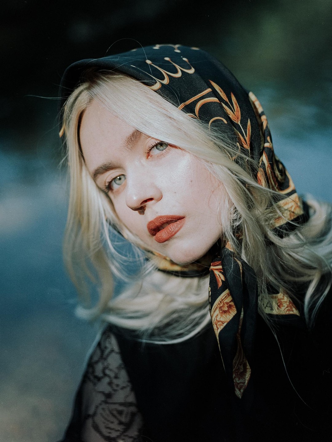 A woman with blonde hair and a patterned headscarf looks towards the viewer.