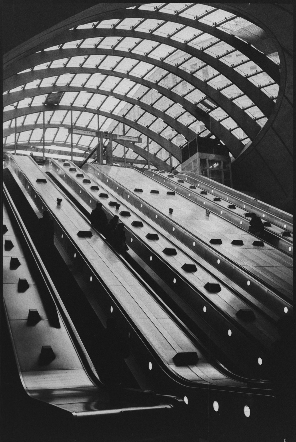 People ride escalators under a glass and metal arched roof.