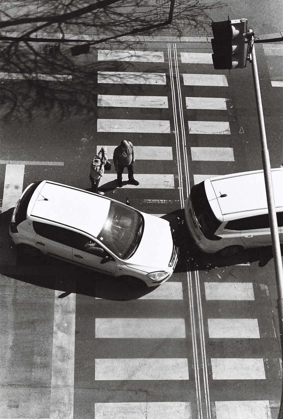Two cars have collided at a crosswalk where two men are standing, viewed from above.