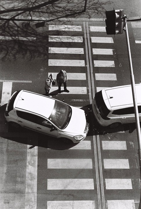 Two cars have collided at a crosswalk where two men are standing, viewed from above.