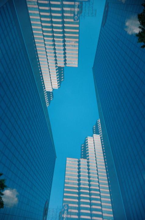 Four tall buildings with many windows are visible from below, with a bright blue sky in the background.