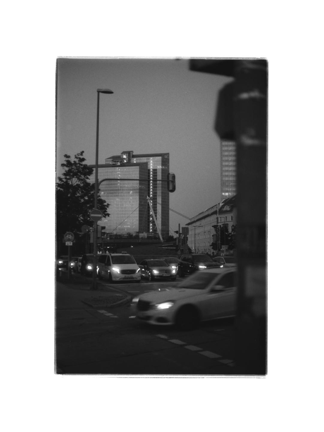 A street scene at dusk shows cars with illuminated headlights and a tall building in the background.