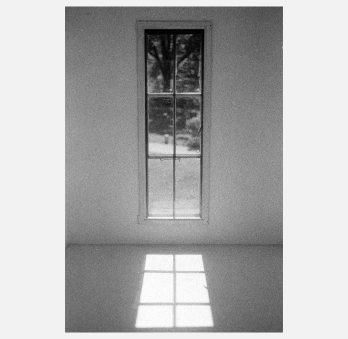 A tall, narrow window with multiple panes is centered on a white wall, casting a grid of light onto the floor.