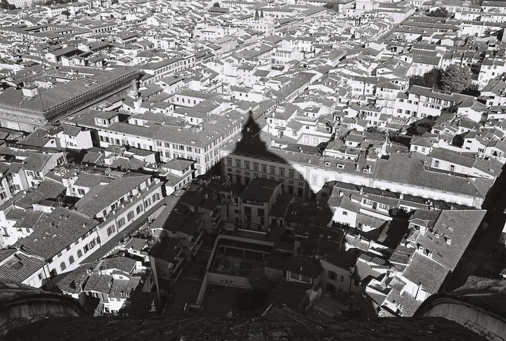 An aerial view shows a city with many buildings and a large shadow cast over them.