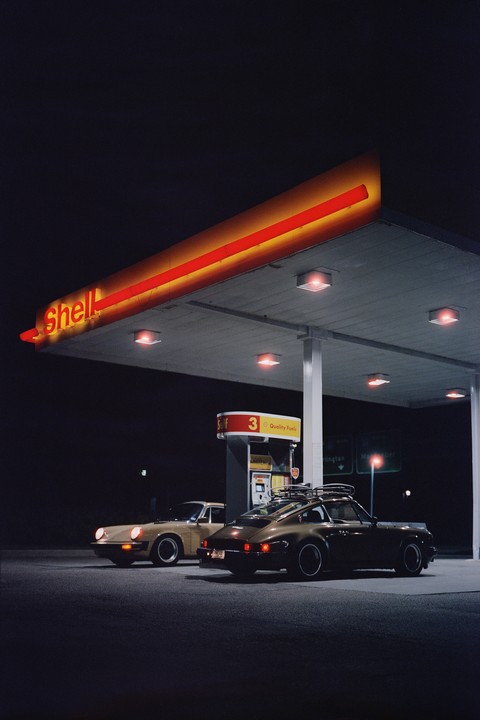 Two cars are parked at a Shell gas station at night.