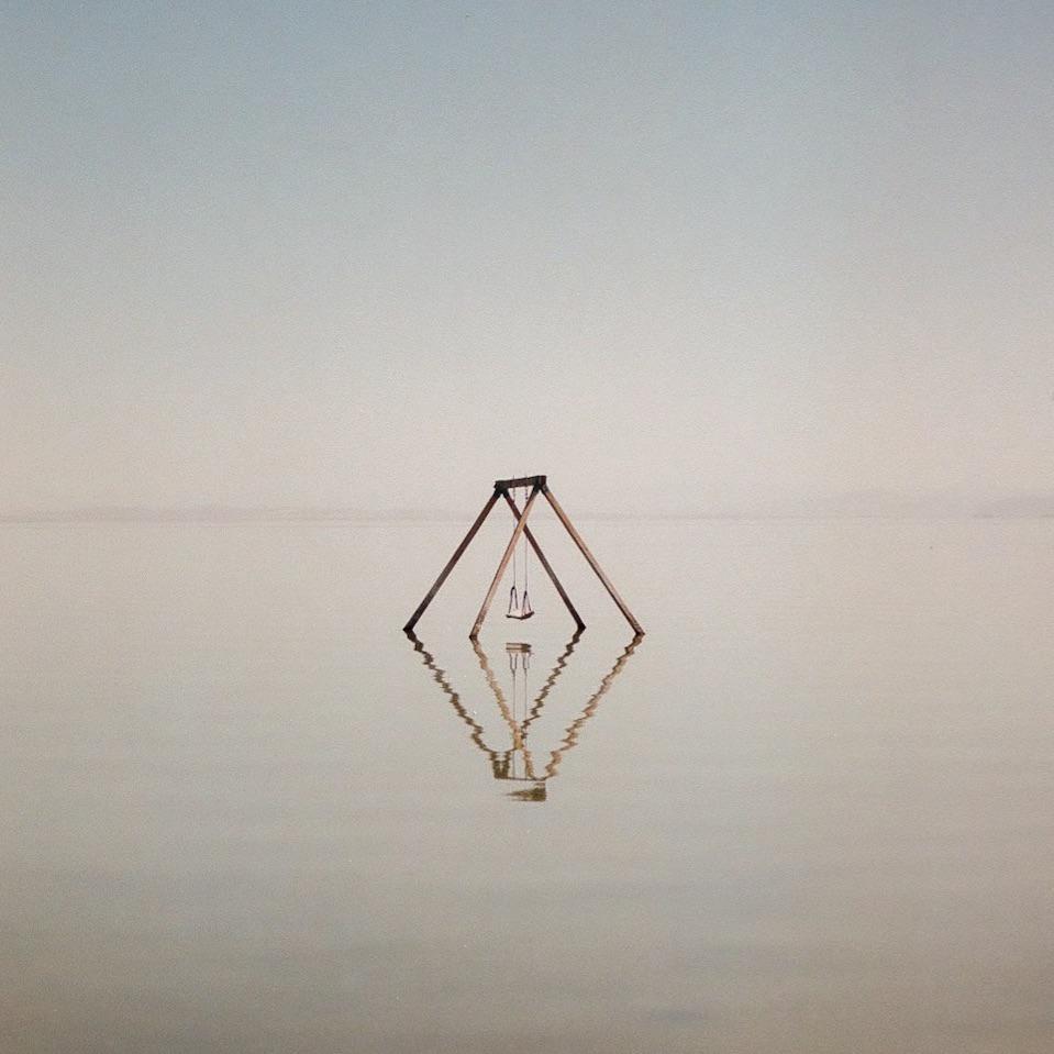 A swing set stands in the middle of a body of water, reflecting on the surface.